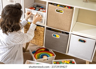 Woman mother applying paper sticker with name title on basket container clean out of childish toys comfortable storage. Female housewife organizing domestic space for kids use print mark tag