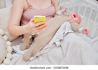 A Woman Mother Breastfeeding A Crying Infant Baby With A Phone In Her Hand. Mom Problems With Breastfeeding And Finding A Solution On The Internet