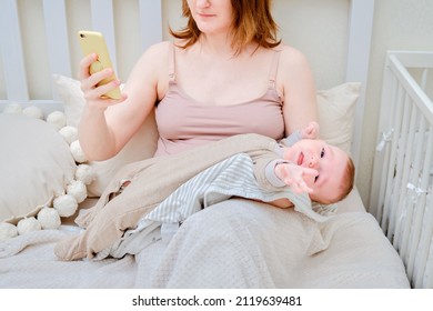 A Woman Mother Breastfeeding A Crying Infant Baby With A Phone In Her Hand. Mom Problems With Breastfeeding And Finding A Solution On The Internet