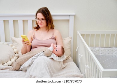 A Woman Mother Breastfeeding Infant Baby With A Phone In Her Hand. Mom Problems With Breastfeeding And Finding A Solution On The Internet