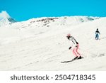 Woman mother skier with child son boy on the piste ski downhill fast motion in Alps. Active winter holidays, skiing downhill in sunny blue sky day. Ski rides on the track with swirls of fresh snow