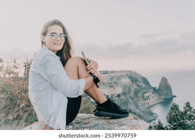 Woman, Mountain, Sunset: Smiling girl sits on a rocky clifftop overlooking the ocean during a golden sunset. - Powered by Shutterstock