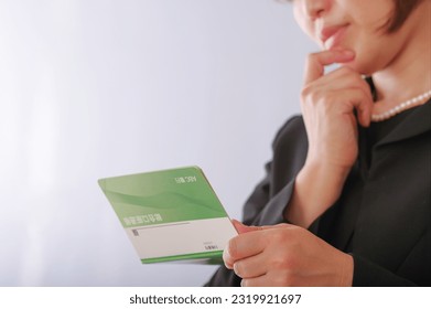 A woman in mourning clothes staring at the passbook.
						
						The bankbook contains "ABC Bank" and a fictitious bank name in Japanese, and the account name is written as "savings account" in Japanese.