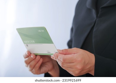 A woman in mourning clothes staring at the passbook.
						
						The bankbook contains "ABC Bank" and a fictitious bank name in Japanese, and the account name is written as "savings account" in Japanese.