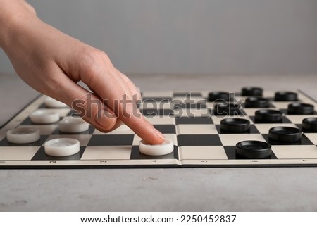Woman moving checker on board at light grey table, closeup