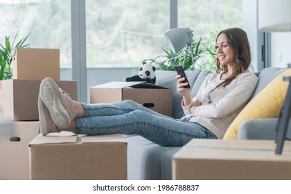 Woman Moving In Her New Home, She Is Sitting On The Couch And Connecting With Her Smartphone