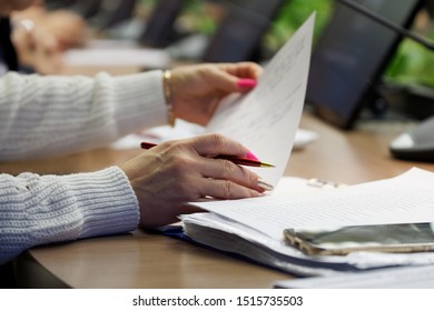 A Woman With Multi-colored Manicure Is Sorting Through Papers While Sitting At Her Desk During A Meeting. Close-up. Shallow Depth Of Field.