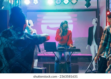 Woman musician using dj controller while performing on stage in nightclub. African american disc jokey playing and mixing electronic music during concert disco party in club - Shutterstock ID 2363581631