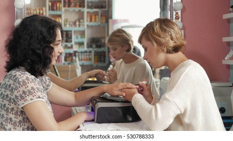 woman in a nail salon receiving  manicure by  beautician with  file.  getting  .   nails to  customer. Blurred background