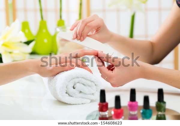 Woman in a nail salon receiving a manicure by\
a beautician