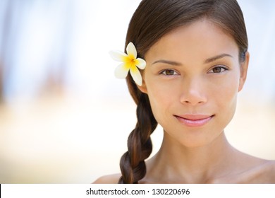 Woman natural beauty portrait of a beautiful and smiling brunette smiling outdoors with a flower in her braided hair. Multicultural Asian / Caucasian girl on health spa wellness travel resort