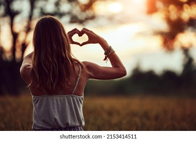 Woman in nature holding heart-shape symbol made with hands.