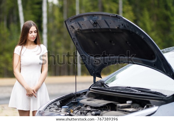 woman near\
broken car looking under opened\
hood