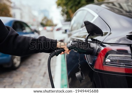 Woman near electric car. Vehicle charged at the charging station.