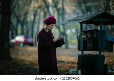 A Woman Near Street Mailboxes Reading A Letter. Eastern Europe.