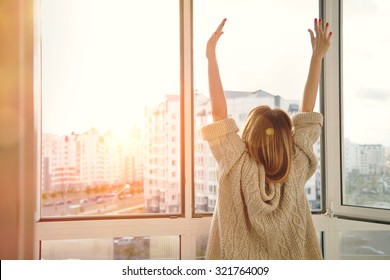 Woman near window raising hands facing the sunrise at morning - Shutterstock ID 321764009