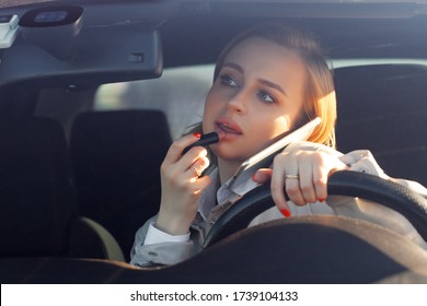 Woman new driver sitting in car, doing make up, using lipstick, talking on phone. Careless and dangerous driving. No concentration on road can cause fatal car accident. Stereotype for women driving