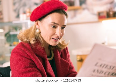 Woman With Newspaper. Elegant Mature French Woman Wearing Beret Reading Newspaper Sitting In Bakery