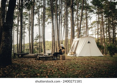 A woman is next to a big white camping tent with camping gears . Taken during golden hour in pine forest during Autumn - Powered by Shutterstock