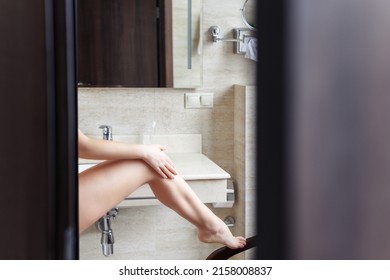 Woman In Nightgown Applying Cream For Protective And Care Dry Skin Legs Standing Against Mirror In Bathroom. 