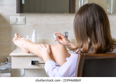 Woman In Nightgown Applying Cream For Protective And Care Dry Skin Legs Sitting On Armchair Against Mirror In Bathroom. 