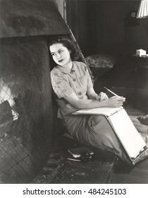 Woman with notebook daydreaming by fireplace