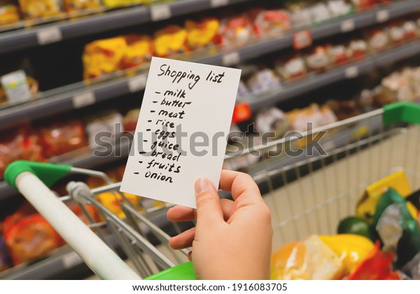 Woman with notebook in\
grocery store, closeup. Shopping list on paper. Check purchases in\
grocery cart.