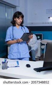Woman Nurse Looking At Digital Tablet Working Late At Night. Medical Assistant Holding Modern Gagdet With Technology For Healthcare System And Medical Practice, Doing Overtime Work At Office.