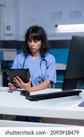 Woman Nurse Looking At Digital Tablet For Practice At Night. Medical Assistant Using Modern Device With Technology And Touch Screen For Healthcare, Working Late. Physician With Job