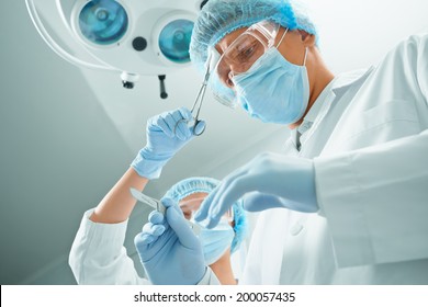 Woman nurse rubs forehead of man surgeon on operation on background of surgical lamp. Point of view shot