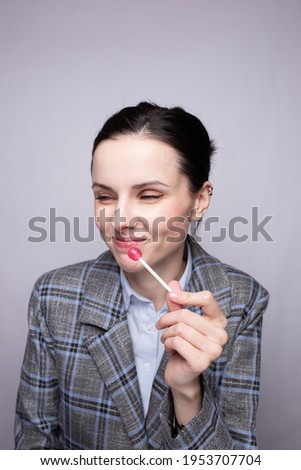 Woman office worker in gray plaid suit eating lollipop, gray studio background