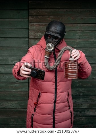 Woman with old gas mask takes a selfie with a mobile phone. Concept - Nuclear Disarmament and Radiation Protection, epidemic, coronavirus, covid-19, pandemic.