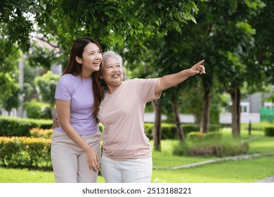 A woman and an older woman are standing in a park, pointing at something. The older woman is wearing a pink shirt and the younger woman is wearing a purple shirt. Scene is happy and friendly - Powered by Shutterstock