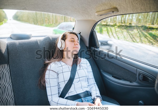 woman on back seat of car. car travel concept.\
listing music with\
headset.