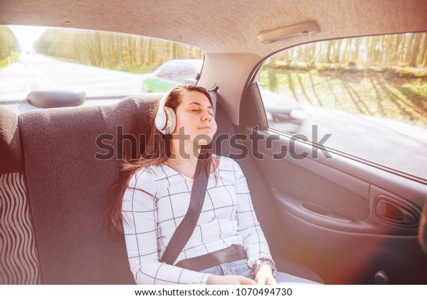 woman on back seat of car. car travel concept.\
listing music with\
headset.