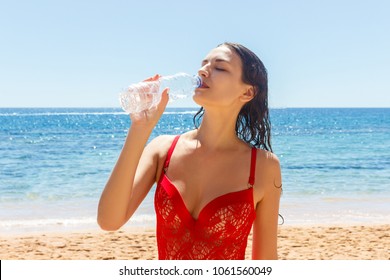 woman on the Beach drinking a cold water in bottle. Female in red bikini enjoying Ice water drink smiling happy laughing.