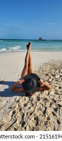 Woman On A Beach With Legs In The Air Wearing A Large Sun Hat.