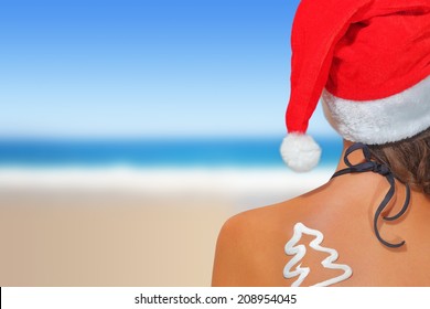 Woman on the beach in santas hat with Christmas tree shaped sunscreen