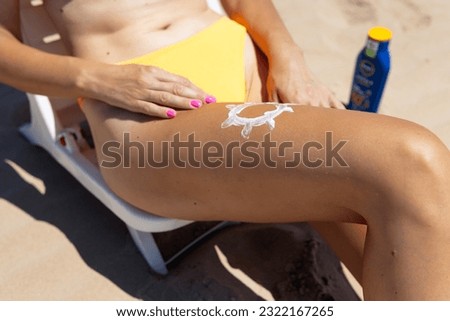 Woman on the beach, the sun is drawn on her leg with sunscreen.the concept of sun protection there is a place for an inscription