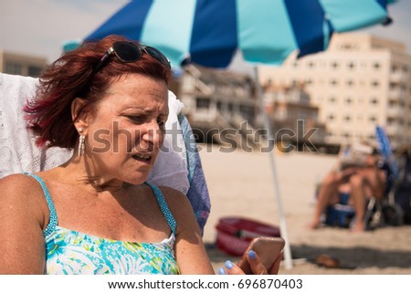 Woman on beach upset by what she is reading on her smartphone