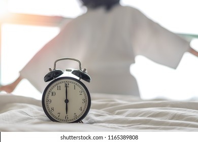 Woman on bed wake up stretching in bedroom with alarm clock at 6.00 a.m. morning. Biological Clock healthcare lifestyle concept - Shutterstock ID 1165389808