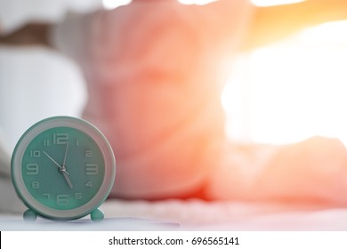 Woman on bed wake up stretching in bedroom with alarm clock at 5.00 a.m. morning. Biological Clock healthcare concept