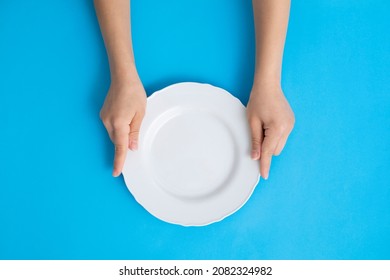 Woman On Blue Background Holding Empty Plate With Both Hands