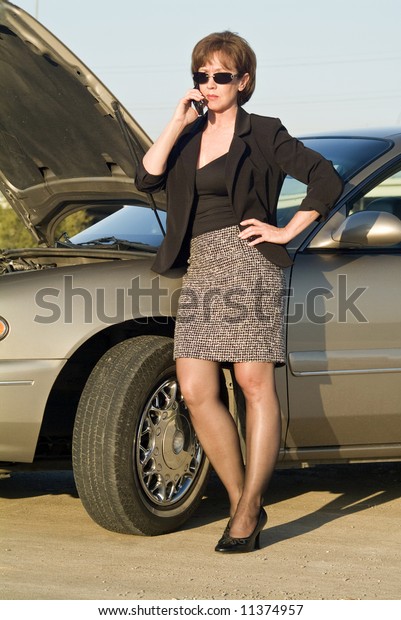 A woman on a cell phone next to a car that\
appears to be out of service.