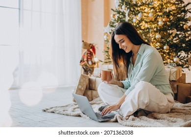 Woman on Christmas using laptop and drinking tea by the Christmas tree - Powered by Shutterstock