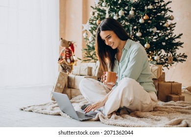 Woman On Christmas Using Laptop And Drinking Tea By The Christmas Tree