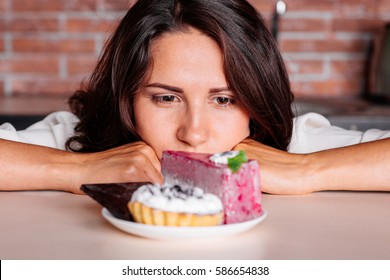 Woman On The Diet Craving To Eat Cake Siting On The Kitchen. Young Attractive Woman Really Wants To Eat Delicious Cake. Diet Concept