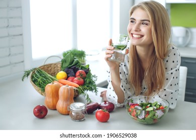 Woman on a diet. Young and happy woman eating healthy salad sitting on the table with green fresh ingredients indoors. High quality photo - Shutterstock ID 1906529038