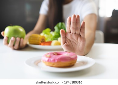 Woman on dieting for good health concept. Close up female using hand push out her favourite donut and choose green apple and vegetables for good health. - Shutterstock ID 1945180816