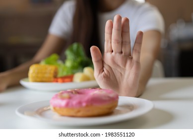 Woman on dieting for good health concept. Close up female using hand push out her favourite donut and choose green apple and vegetables for good health. - Shutterstock ID 1983551120
